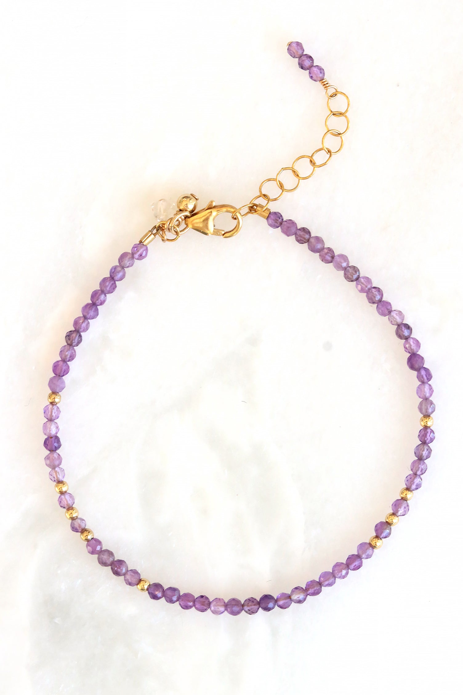 Amethyst birthstone charm bracelet with faceted amethyst beads and gold accents, shown on white background.
