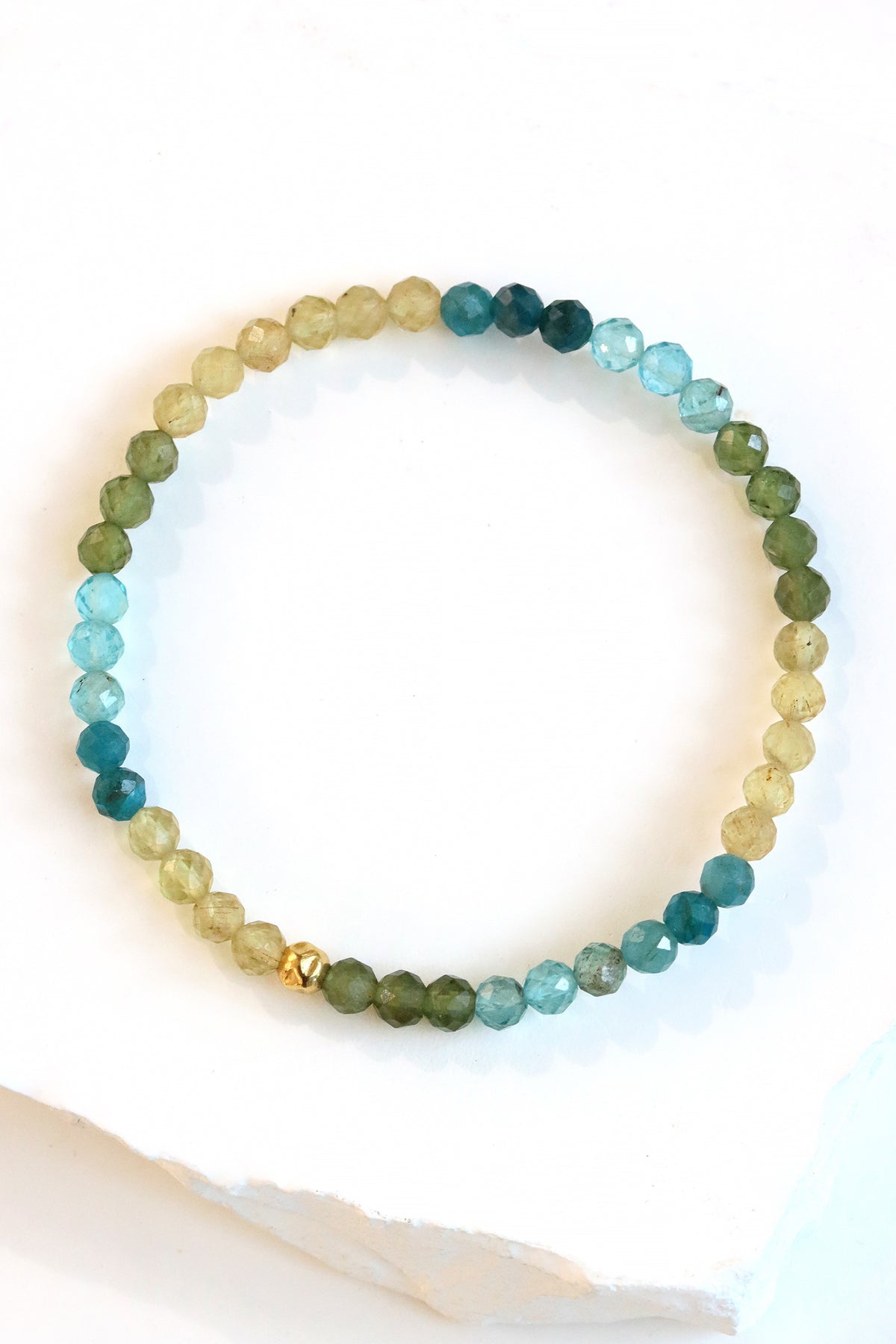 Apatite Petal Bracelet with faceted blue, green, and yellow beads and a gold fill hammered ball accent, styled on wrist with a gold cuff bracelet.