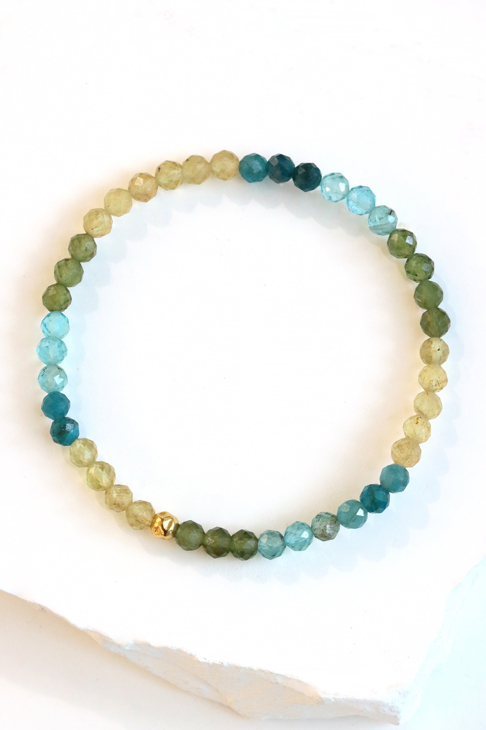 Apatite Petal Bracelet with faceted blue, green, and yellow beads and a gold fill hammered ball accent, styled on wrist with a gold cuff bracelet.