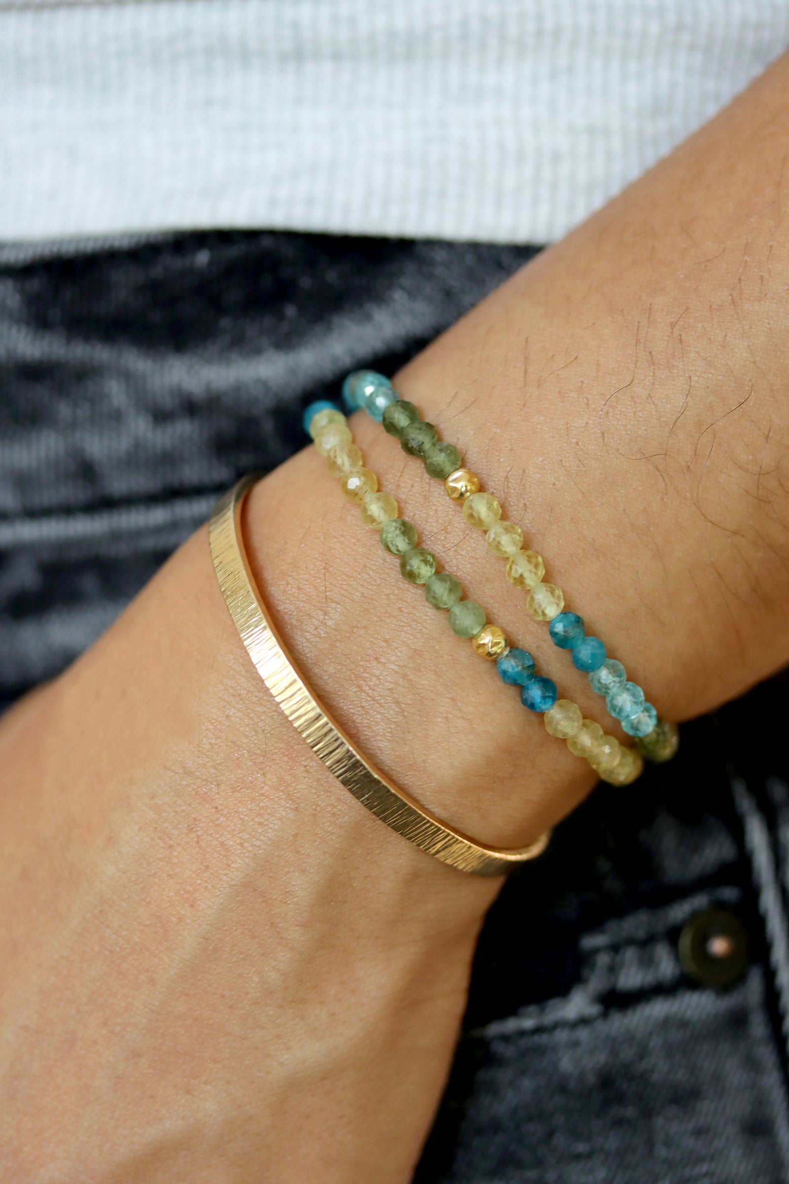 Apatite Petal Bracelet with faceted blue, green, and yellow beads and a gold fill hammered ball accent, styled on wrist with a gold cuff bracelet.