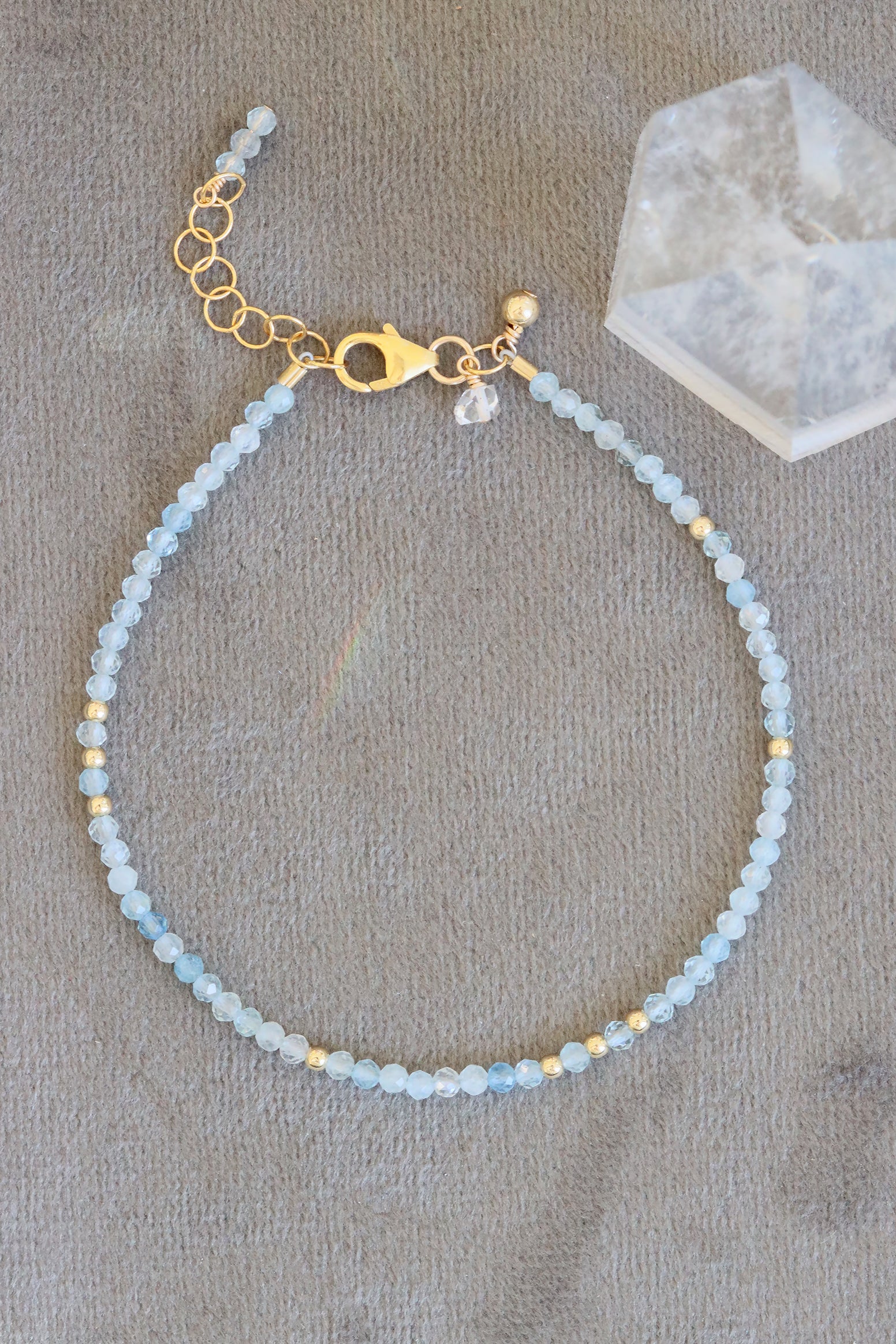 Aquamarine birthstone charm bracelet with faceted aquamarine beads and gold accents, shown on grey background.