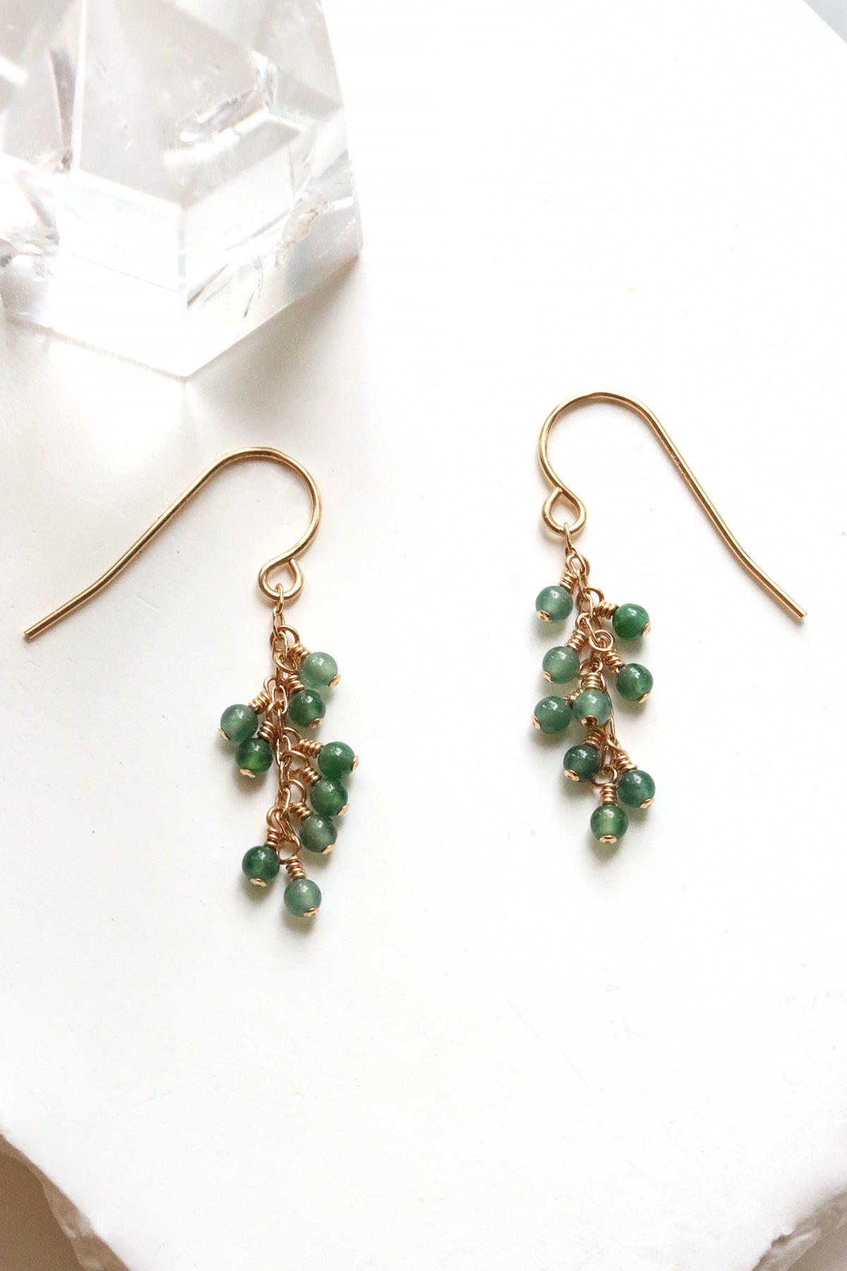 Jade Breeze Earrings with wire-wrapped Guatemalan jade beads on gold hook earrings, on a white surface