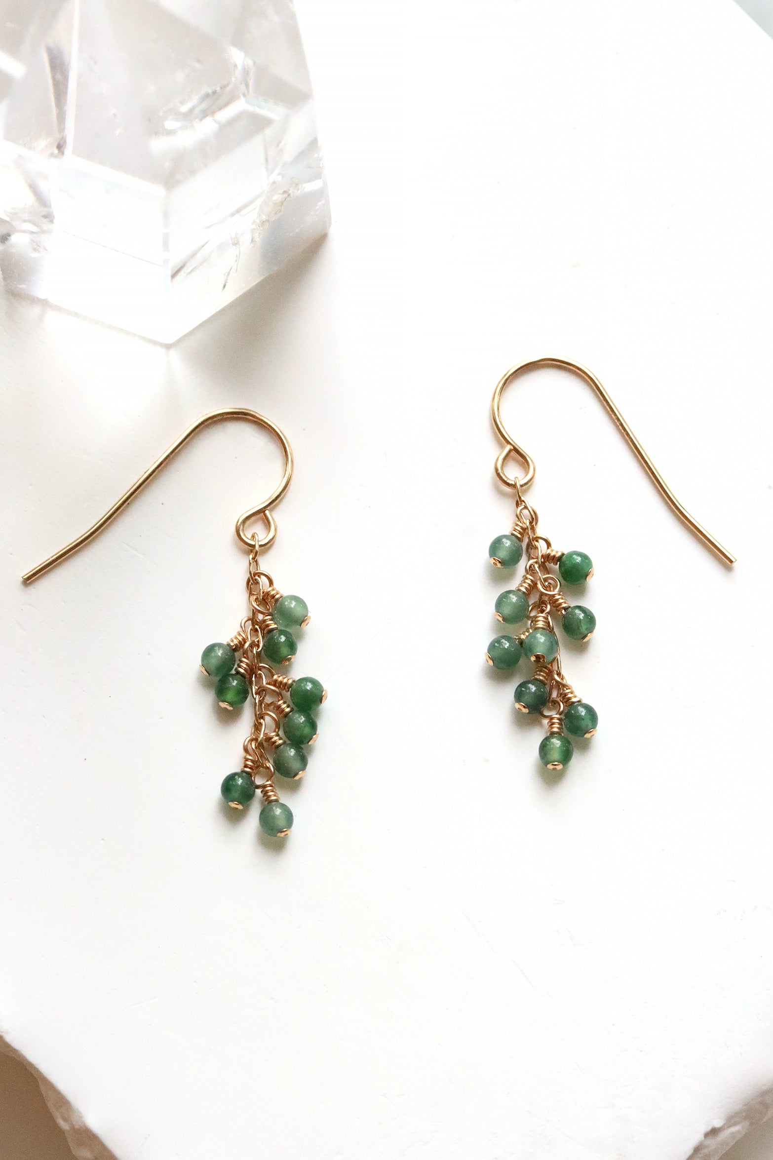 Jade Breeze Earrings with wire-wrapped Guatemalan jade beads on gold hook earrings, on a white surface