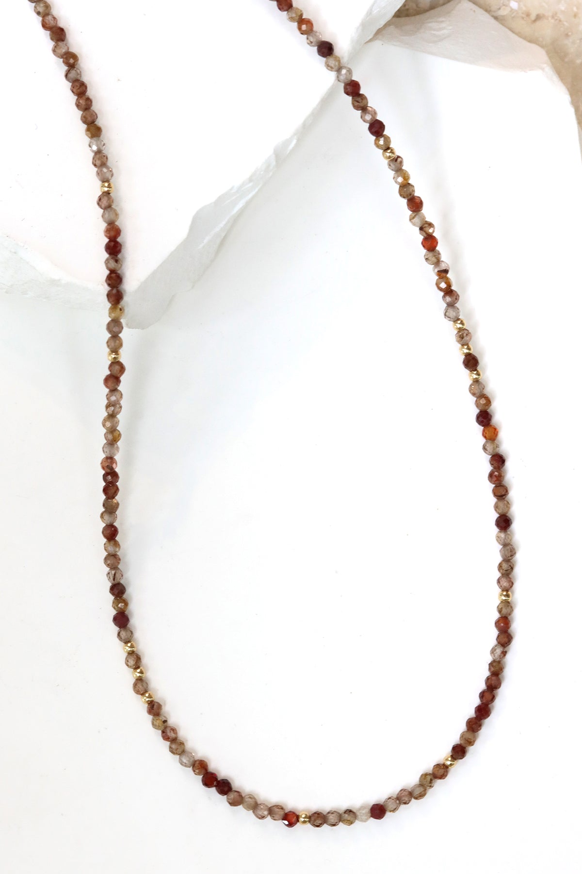 Chocolate zircon Lena necklace with faceted beads in cocoa, honey, and cream tones, draped on natural stone