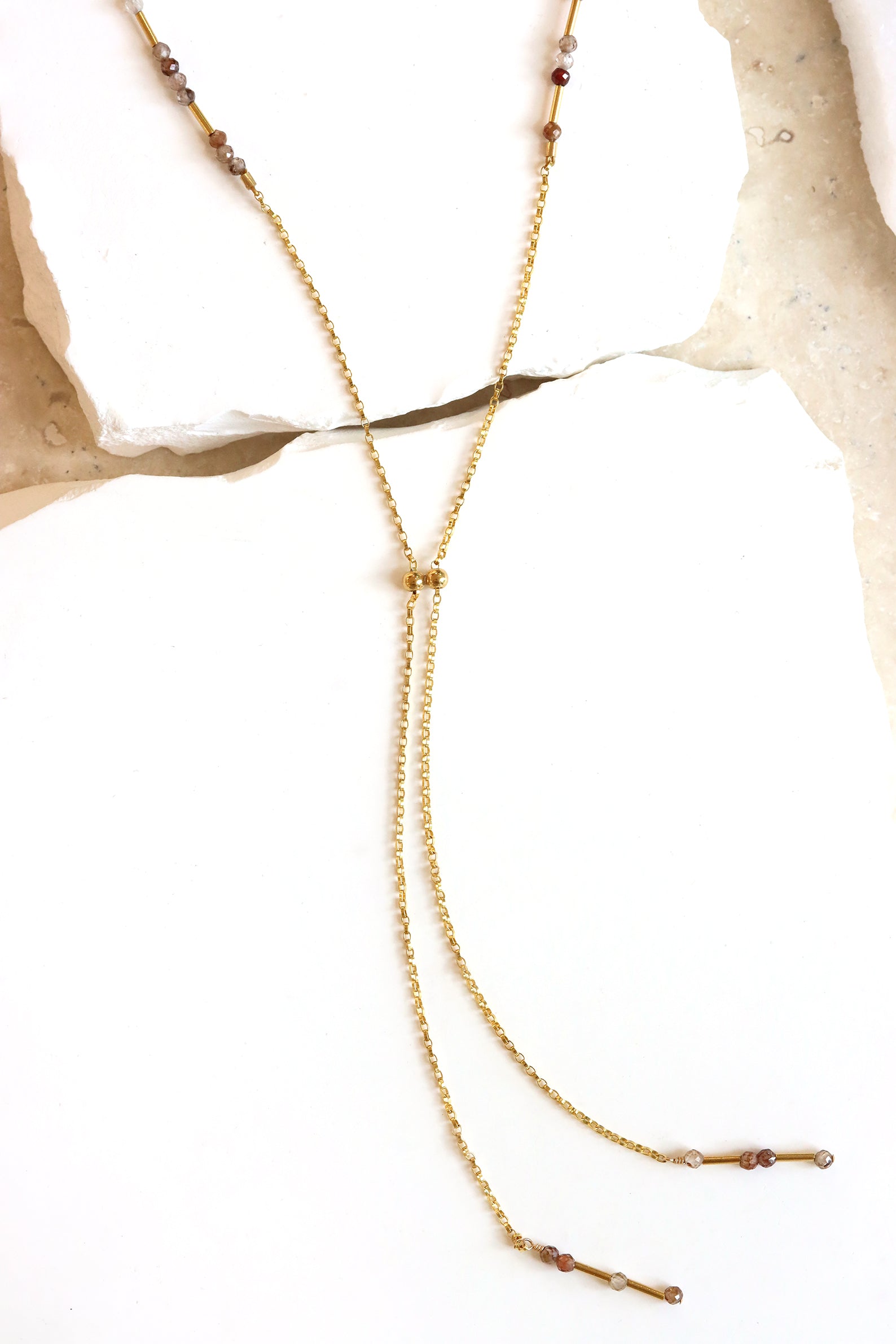 Chocolate zircon lariat necklace with faceted gemstones and liquid gold accents, laid on natural stone