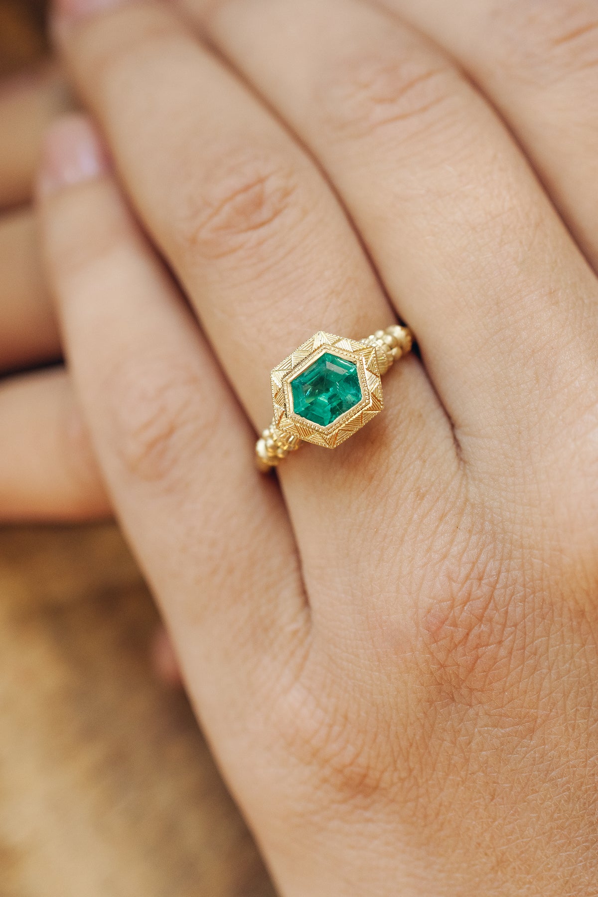 Emerald pedestal solitaire ring in 18k gold with hand-engraved band by Erin Cuff.