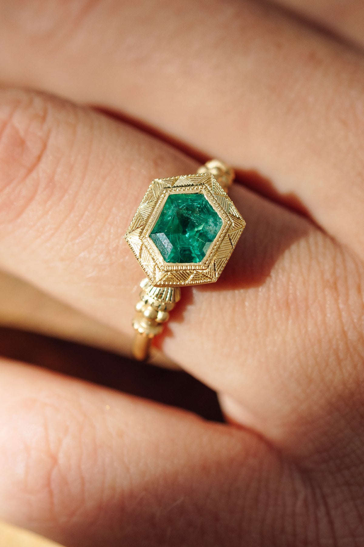 Emerald pedestal solitaire ring in 18k gold with hand-engraved band by Erin Cuff.