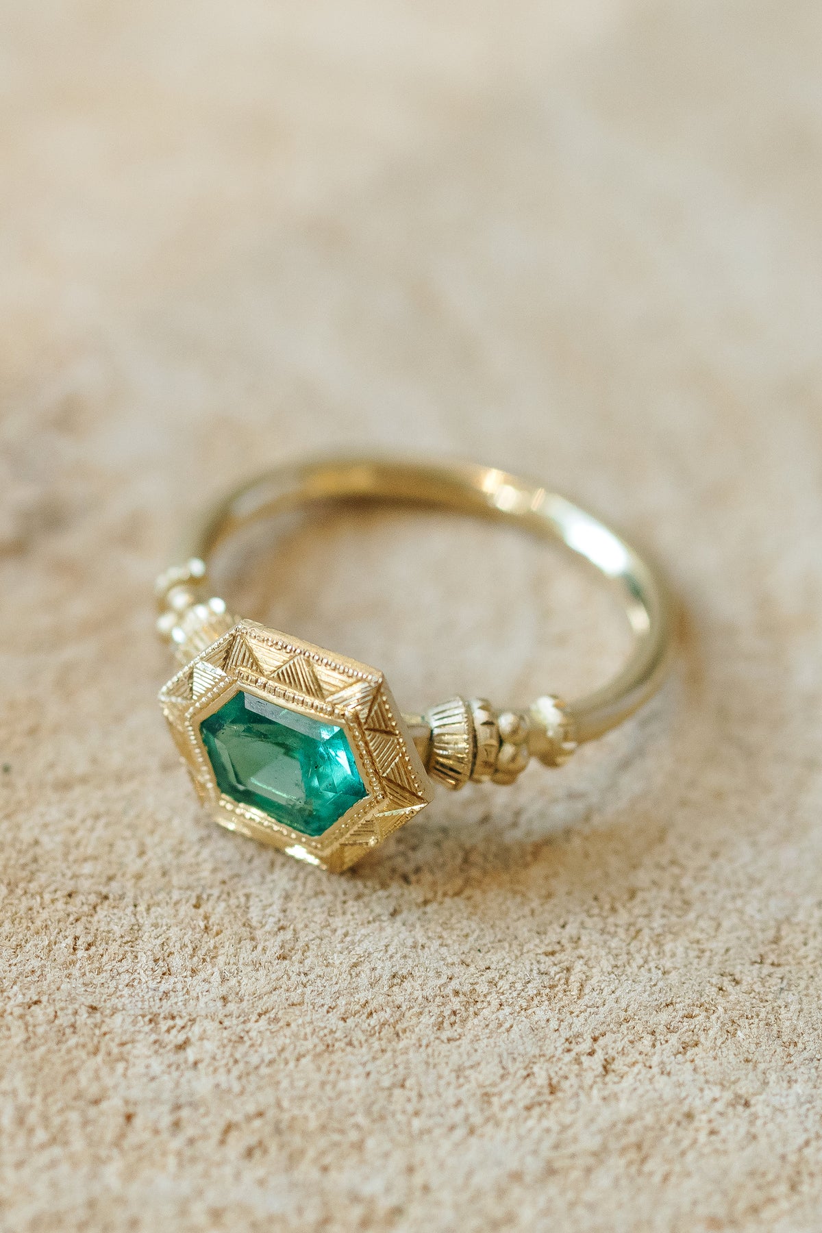 Emerald pedestal solitaire ring in 18k gold with hand-engraved band by Erin Cuff.