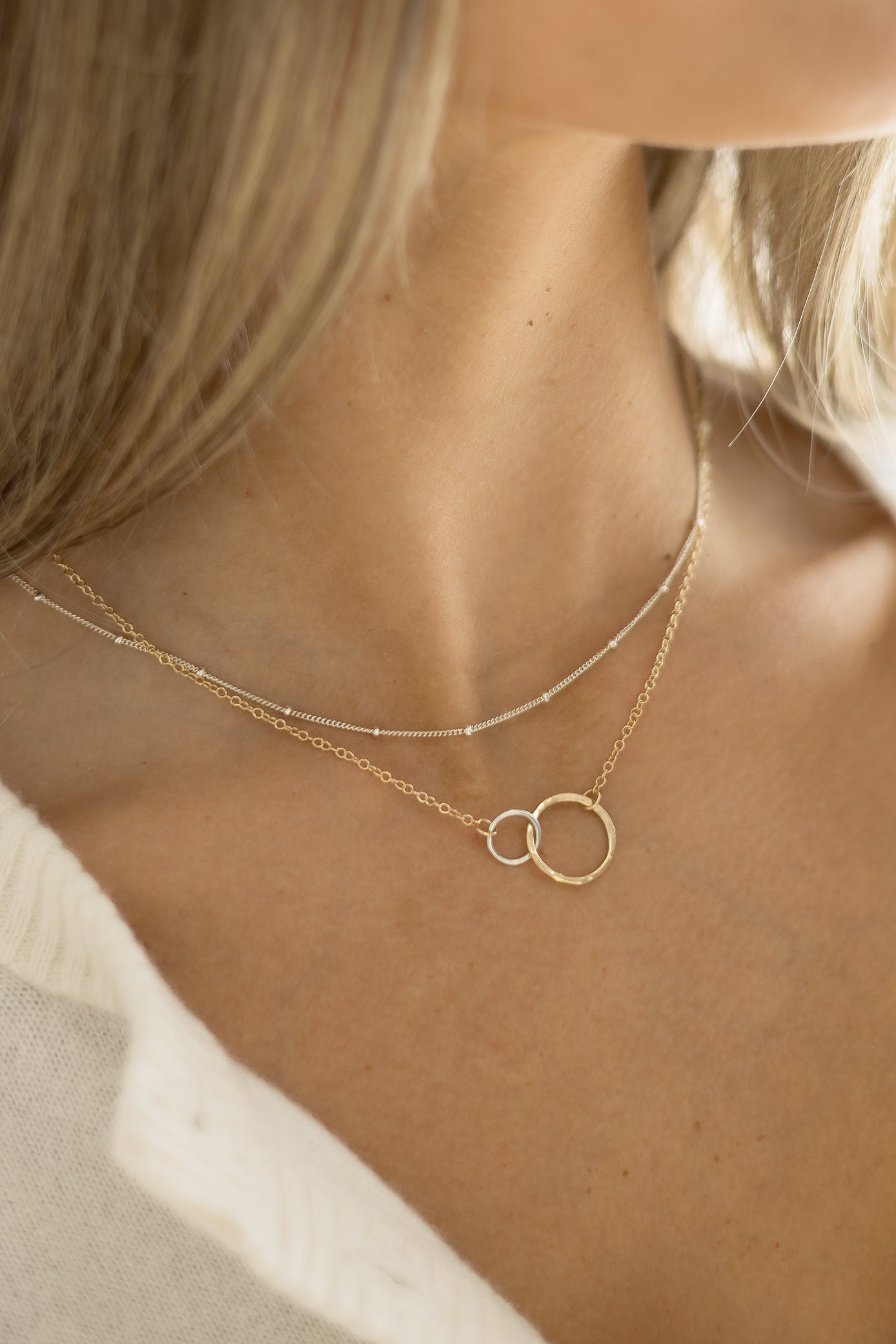 Close-up of the Petite Encircle Necklace featuring two interlocking hand-hammered gold and silver  rings on a delicate gold chain.