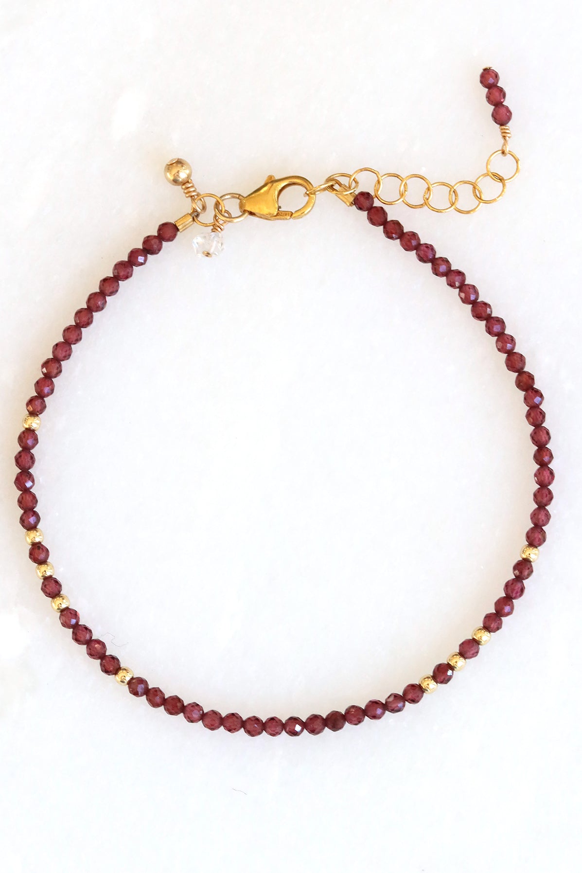 Garnet birthstone charm bracelet with faceted garnet beads and gold accents, shown on white background.