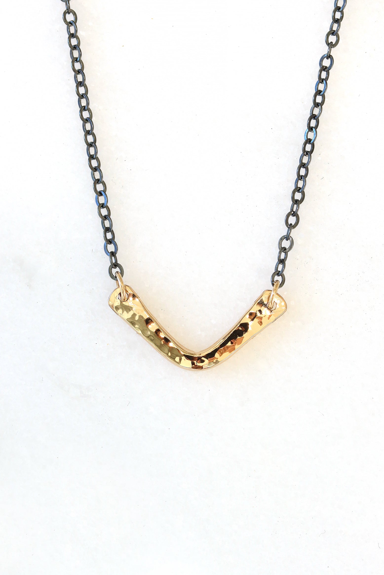 Close-up of the Vela Necklace featuring a hand-hammered gold V-shaped pendant on an oxidized chain.