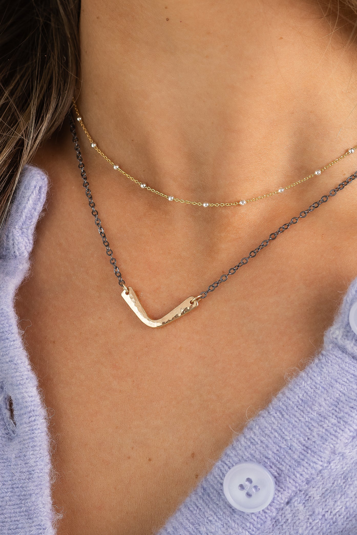 Close-up of the Vela Necklace featuring a hand-hammered gold V-shaped pendant on an oxidized chain.