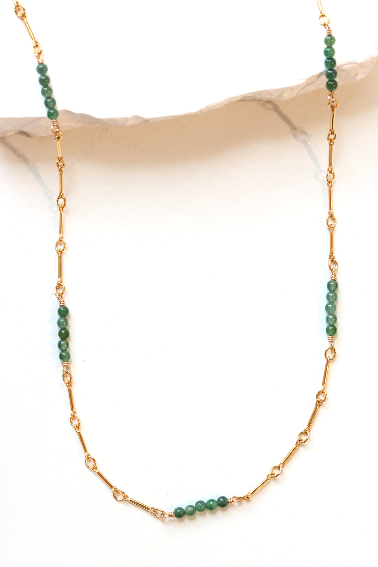Gold necklace with green jade  beads on a beige background