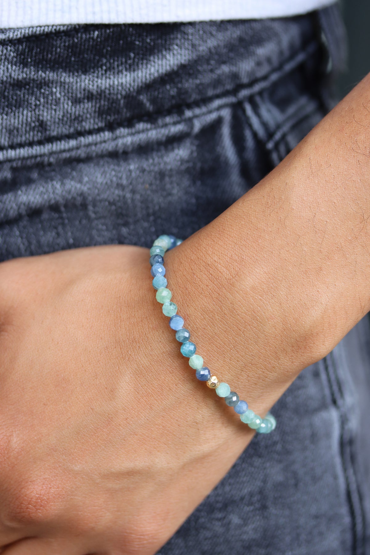 Kyanite Petal Bracelet with faceted blue green beads and a gold fill hammered ball accent, styled on wrist against a denim background.