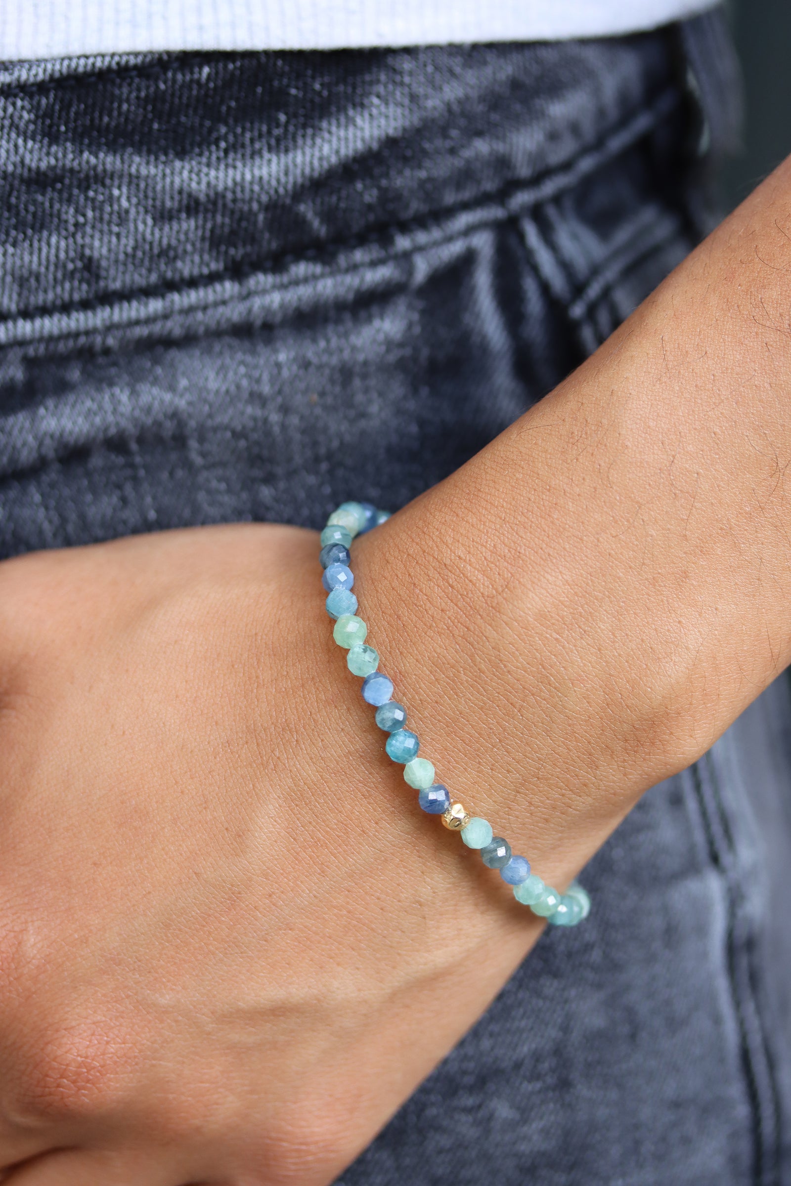Kyanite Petal Bracelet with faceted blue green beads and a gold fill hammered ball accent, styled on wrist against a denim background.