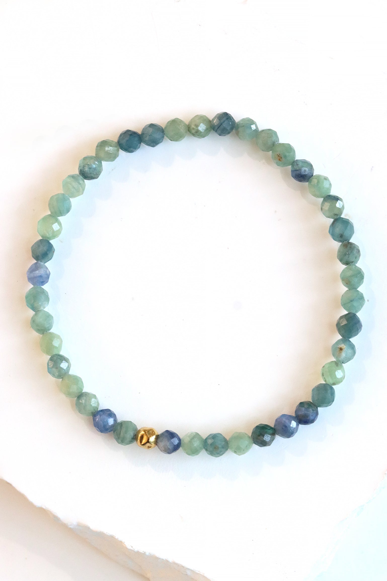 Kyanite Petal Bracelet with faceted blue green beads and a gold fill hammered ball accent, styled on wrist against a denim background.