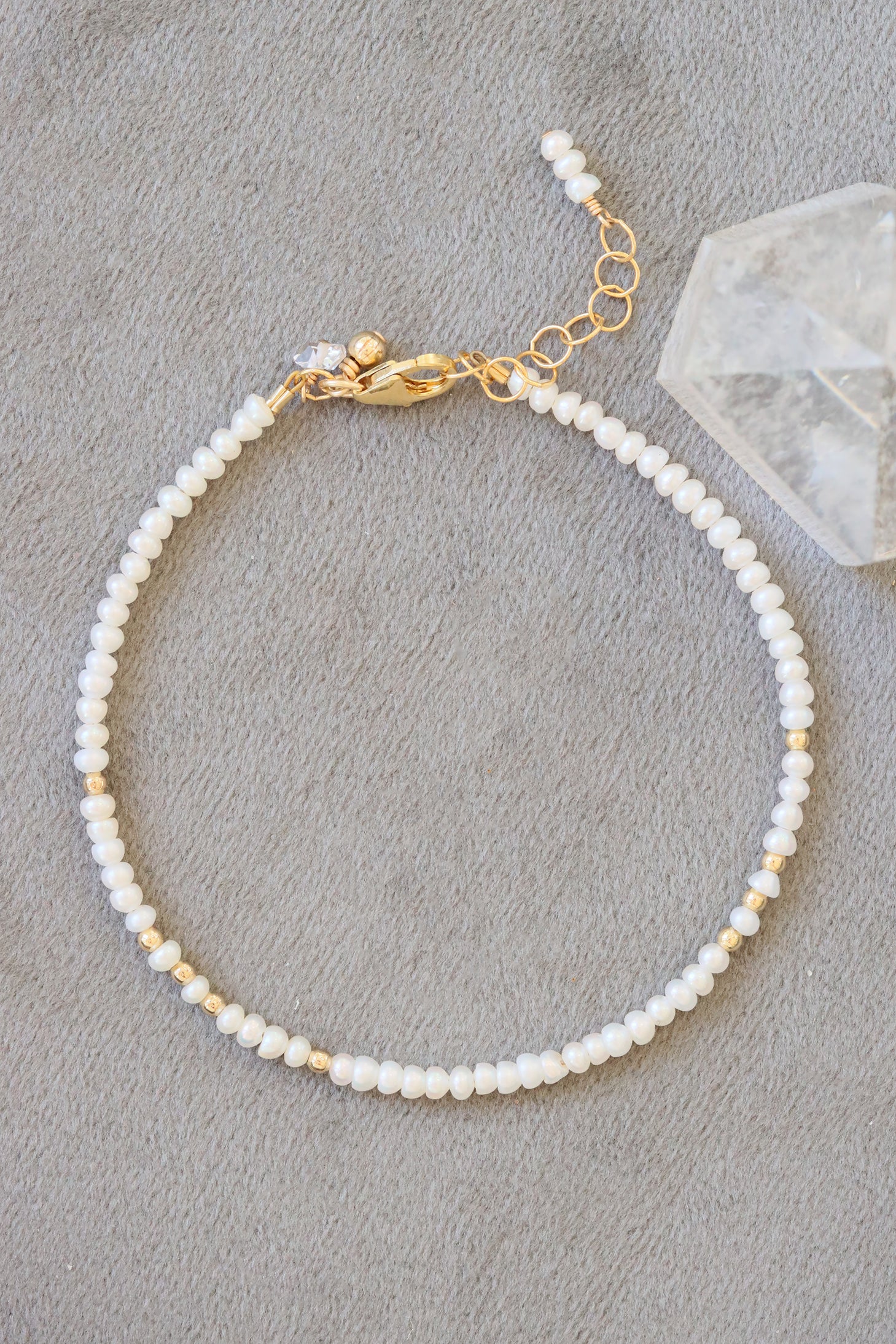 June birthstone charm bracelet with freshwater pearl beads and gold accents, shown on grey background.