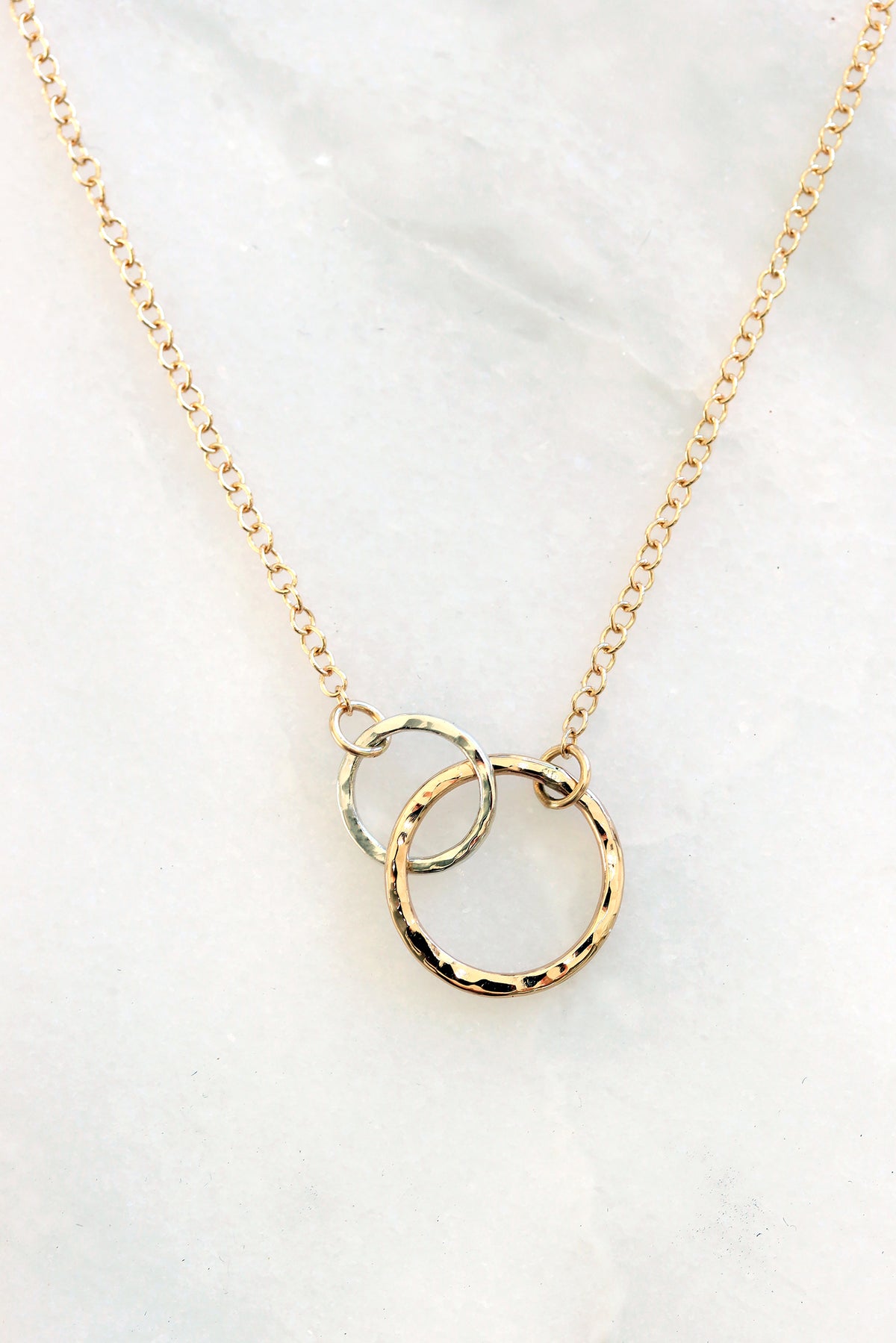 Close-up of the Petite Encircle Necklace featuring two interlocking hand-hammered gold and silver  rings on a delicate gold chain.