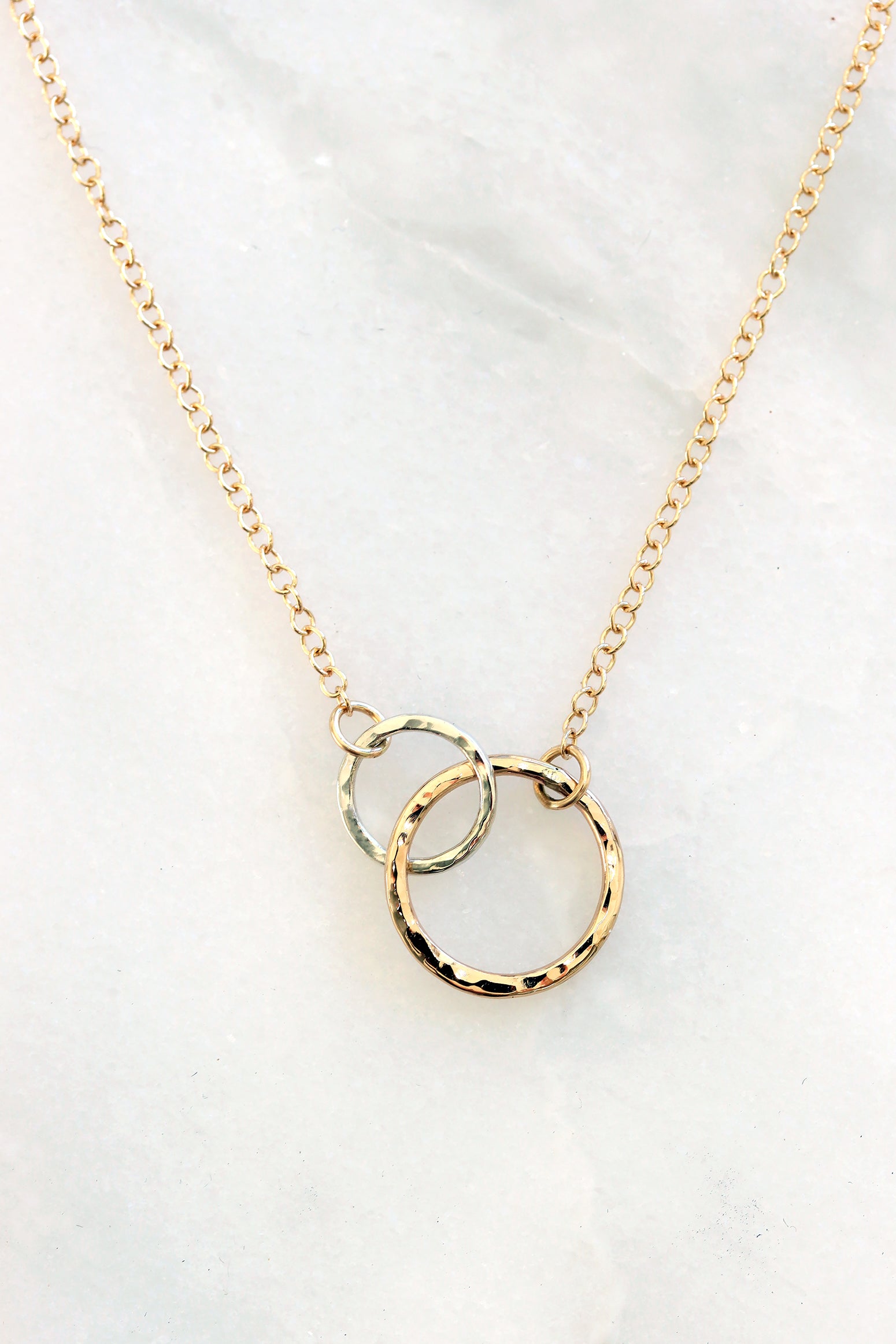 Close-up of the Petite Encircle Necklace featuring two interlocking hand-hammered gold and silver  rings on a delicate gold chain.