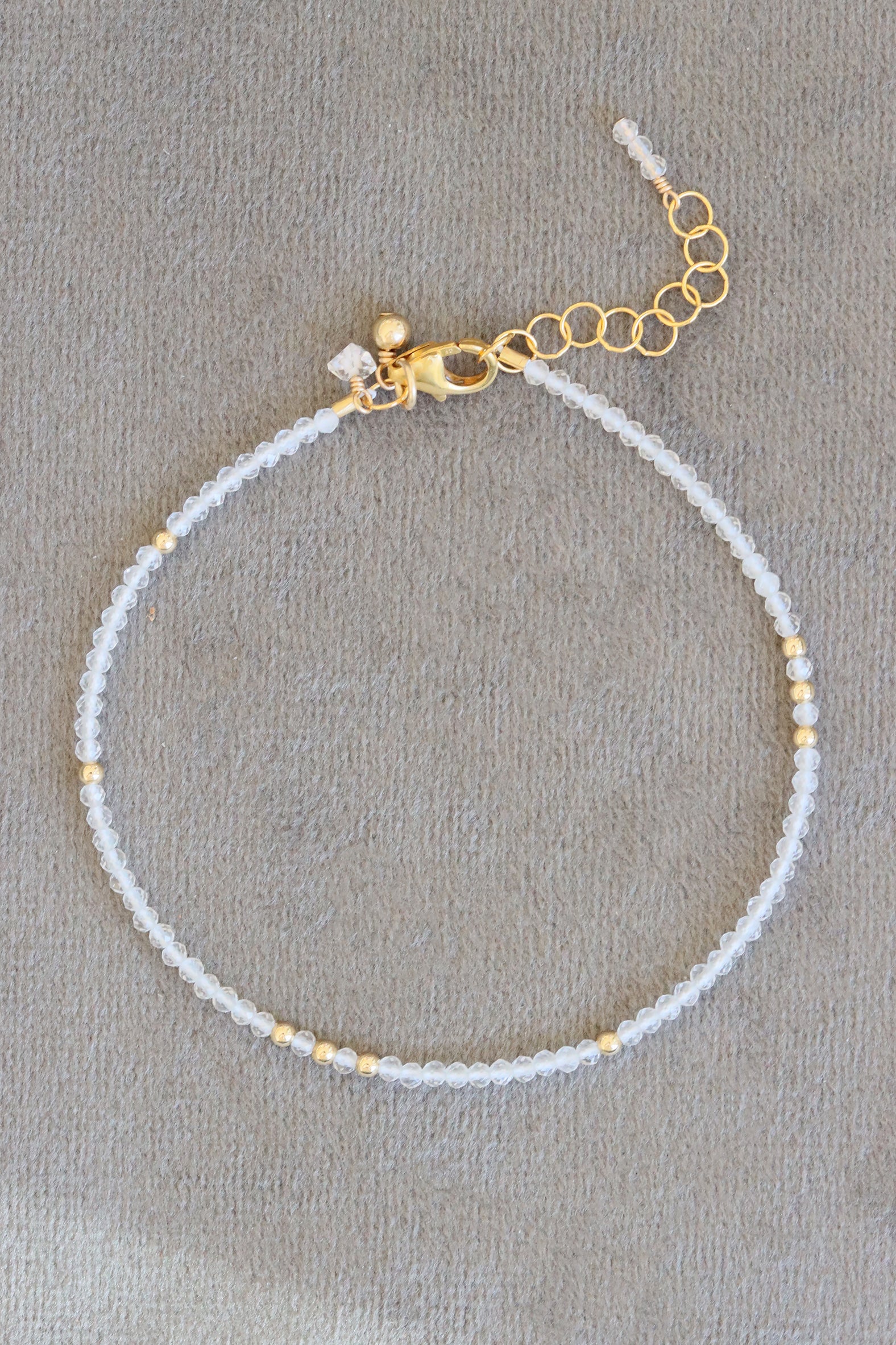 April birthstone charm bracelet with crystal quartz beads and gold accents, shown on white background