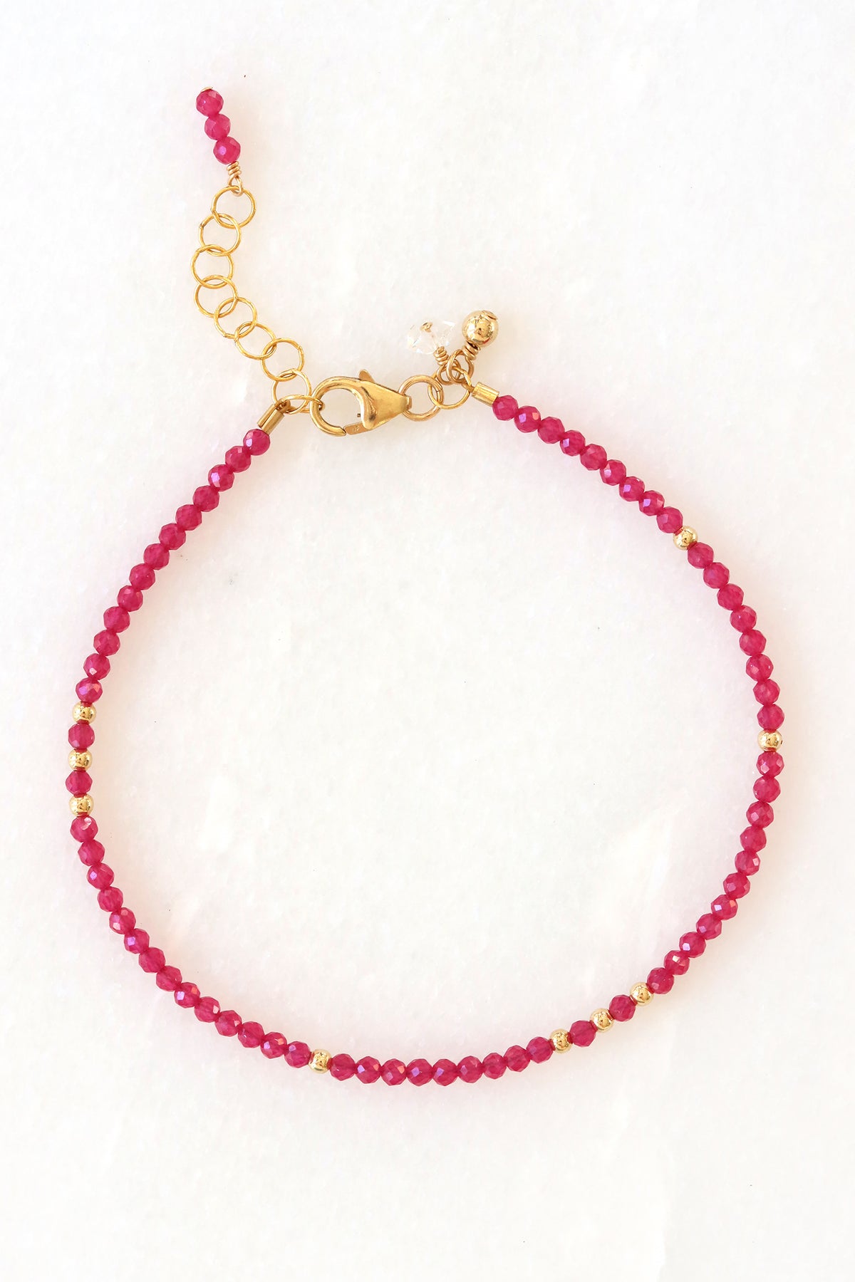 Ruby birthstone charm bracelet with faceted ruby beads and gold accents, shown on white background.
