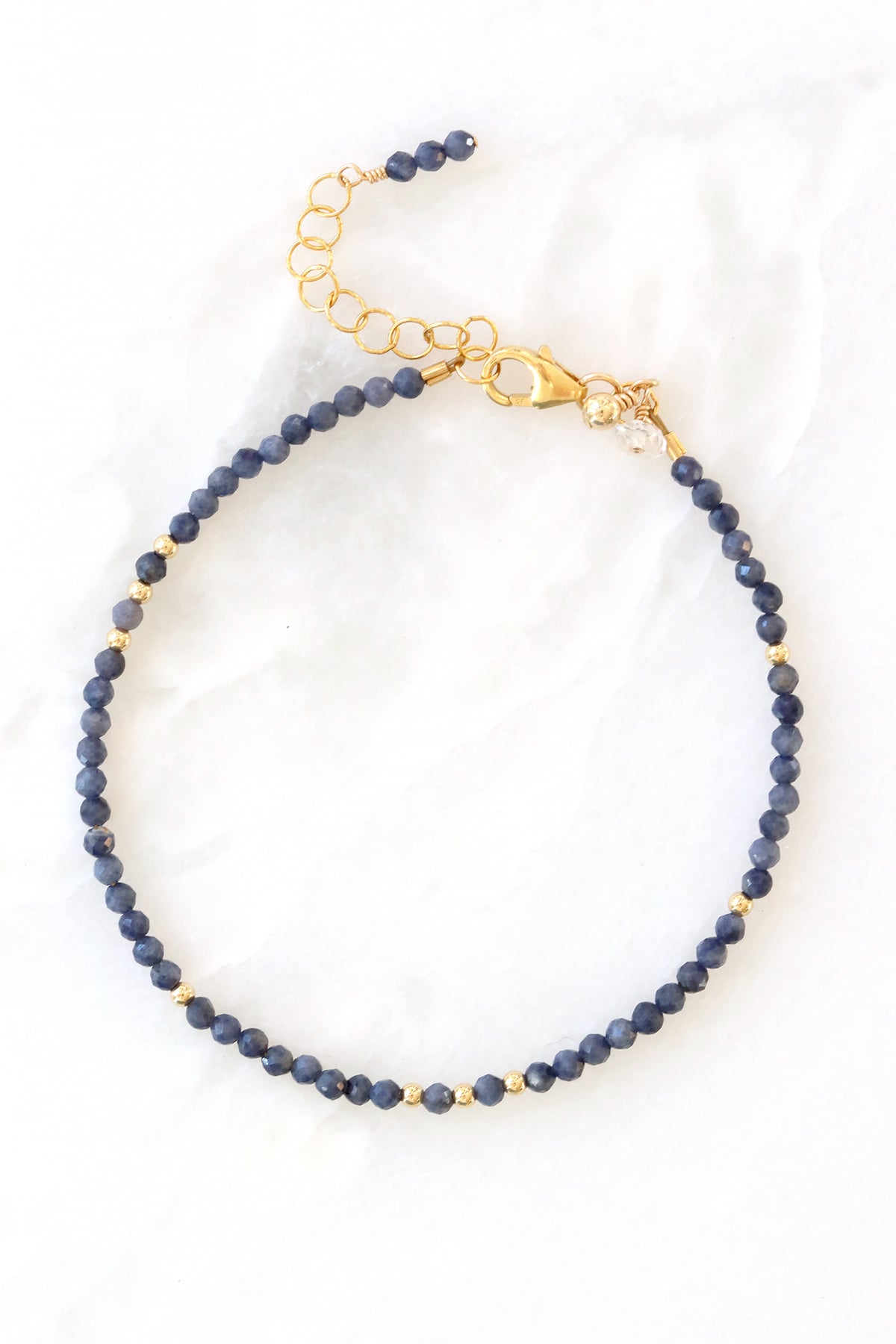 Sapphire birthstone charm bracelet with faceted sapphire beads and gold accents, shown on white background.