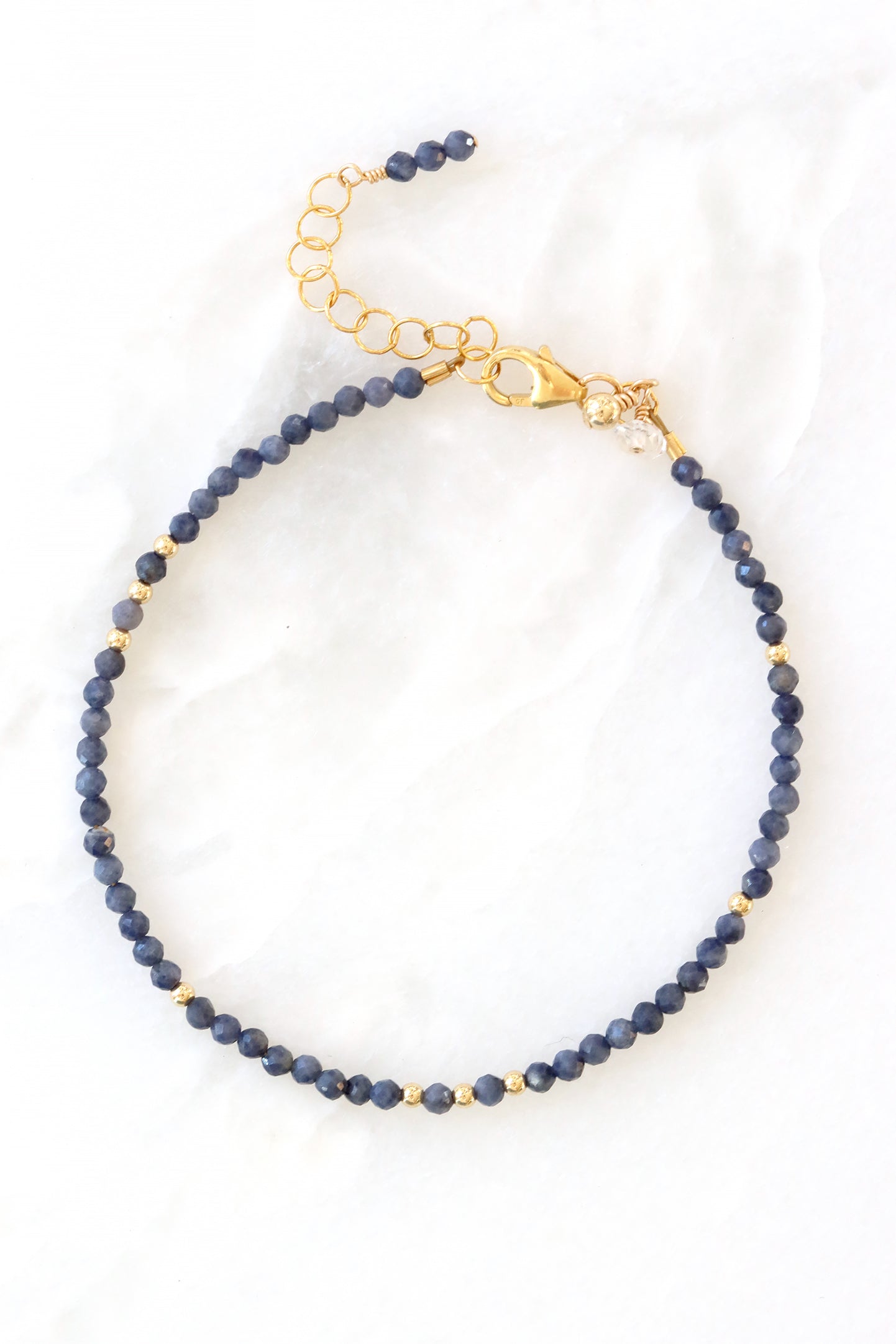 Sapphire birthstone charm bracelet with faceted sapphire beads and gold accents, shown on white background.