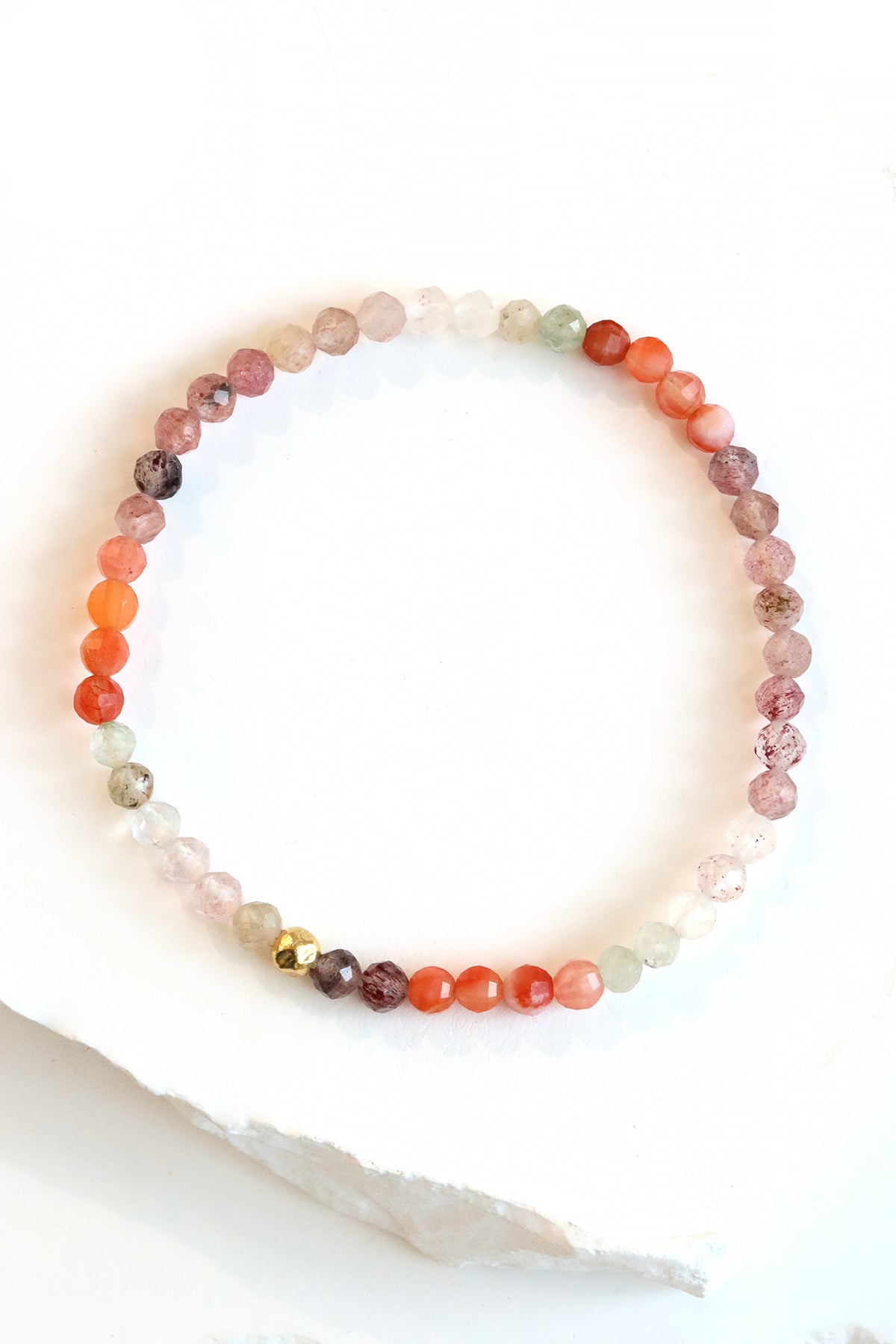 Strawberry Quartz Petal Bracelet with micro-faceted rose quartz, strawberry quartz, and red agate beads in a gradient red blend, with a gold fill hammered ball accent, photographed on a white surface.