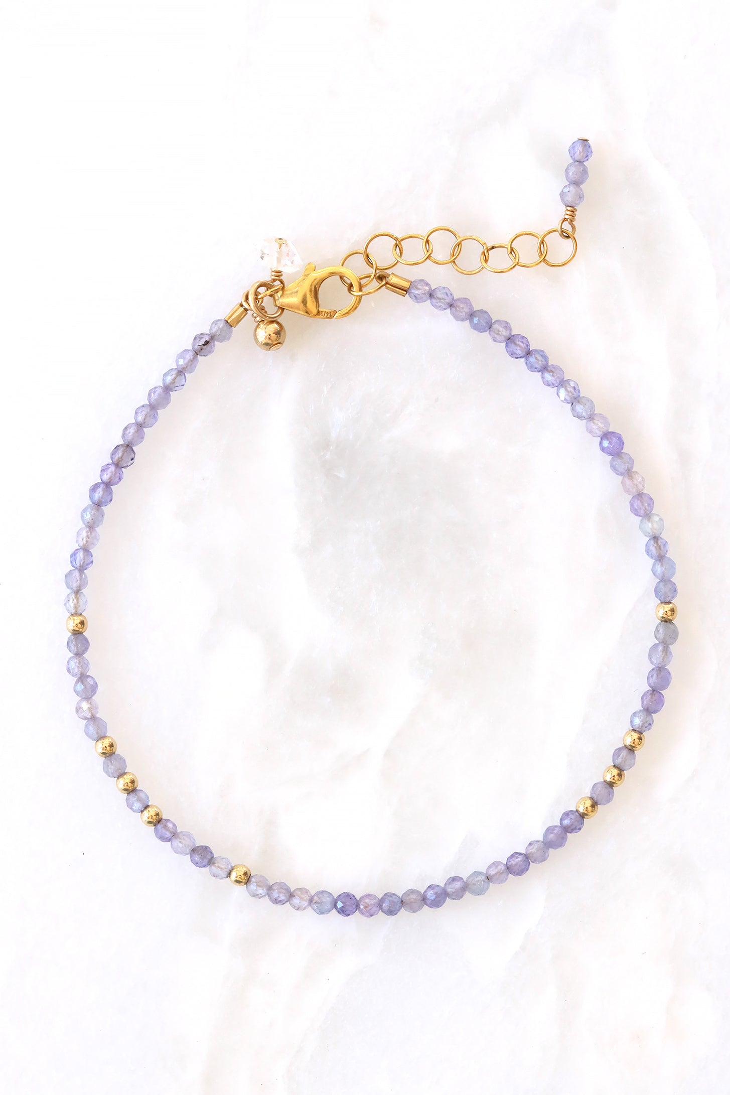 Tanzanite birthstone charm bracelet with faceted tanzanite beads and gold accents, shown on white background.