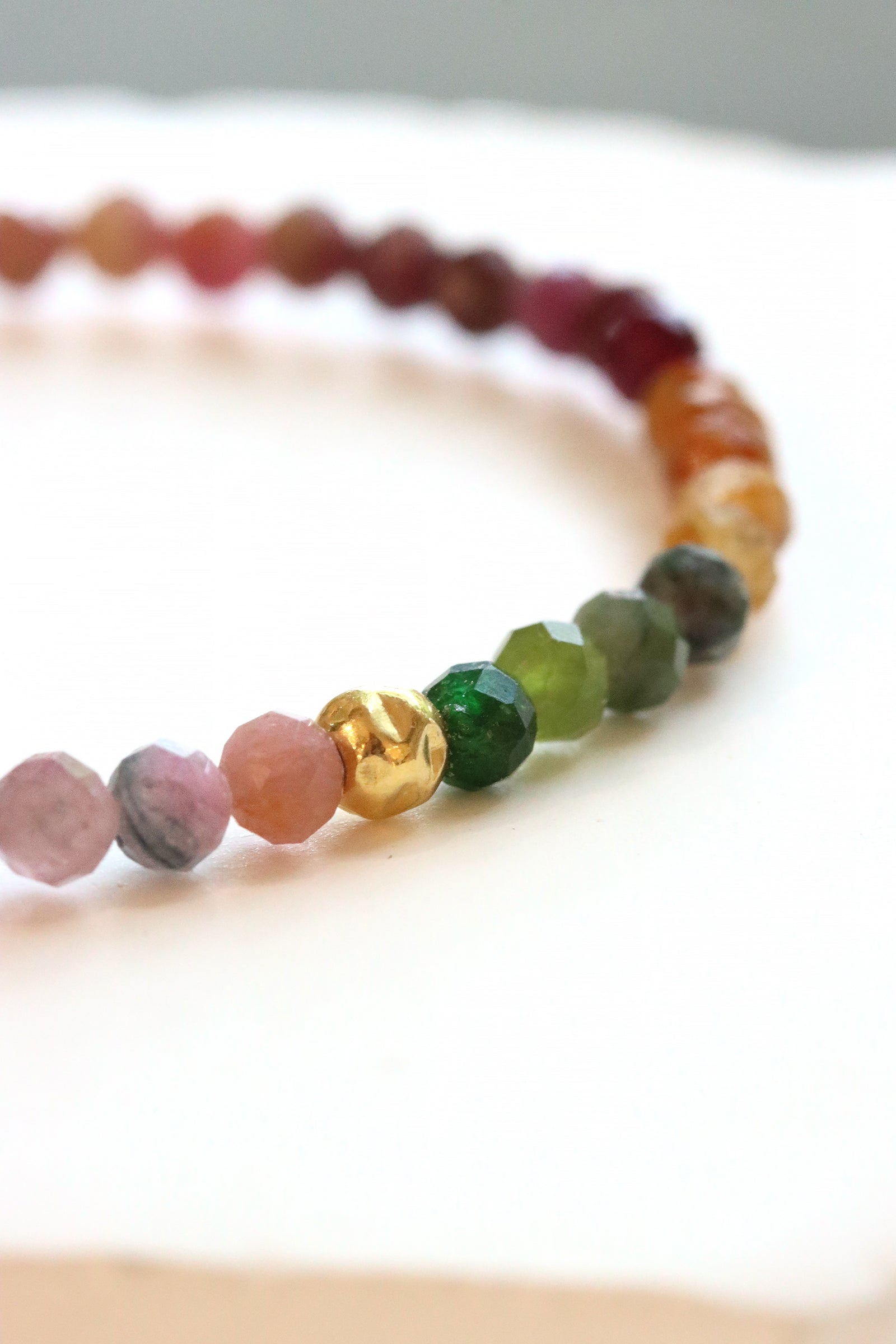 Tourmaline Petal Bracelet with faceted multicolor tourmaline beads in pink, green, and golden tones and a gold fill hammered ball accent, photographed on a white surface.