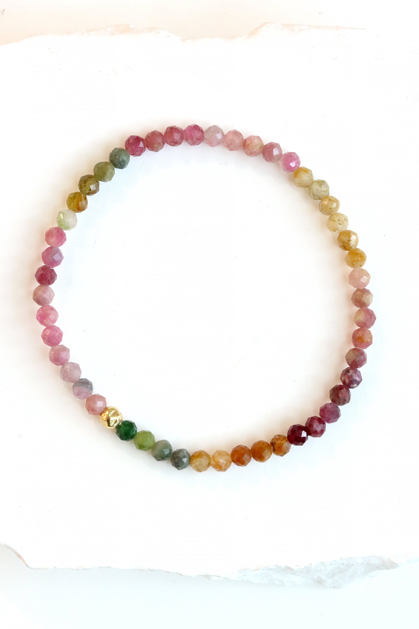 Tourmaline Petal Bracelet with faceted multicolor tourmaline beads in pink, green, and golden tones and a gold fill hammered ball accent, photographed on a white surface.